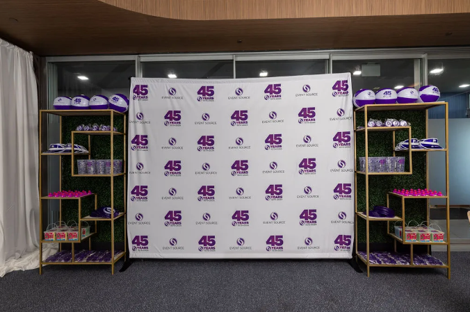 Step and repeat banner with purple company logo set up between two gold bookcases.